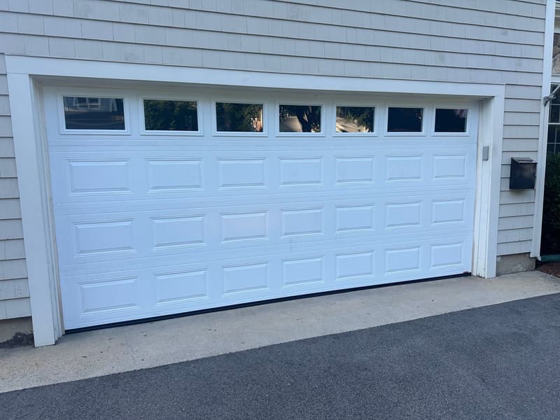 White double raised-panel garage door with top windows on gray shingle home